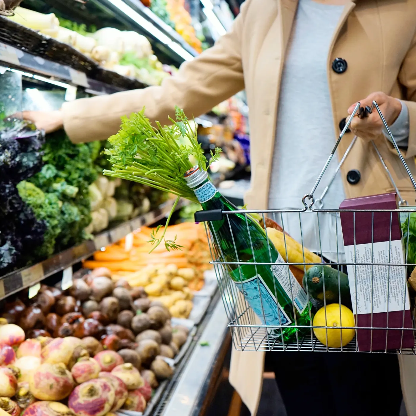 Shopper carrying a basket of groceries past the produce section